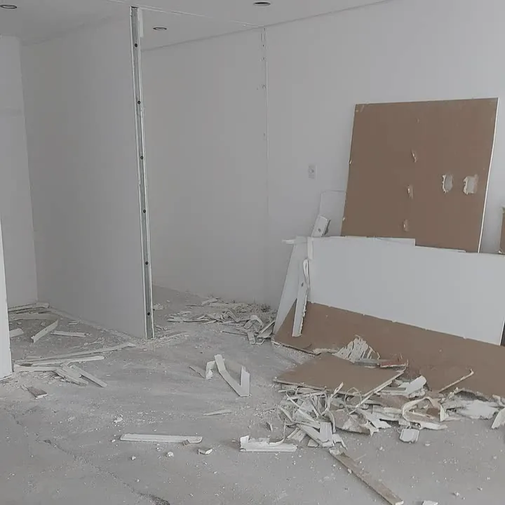 Sala de academia em reforma, com paredes de gesso abertas e entulho no chão