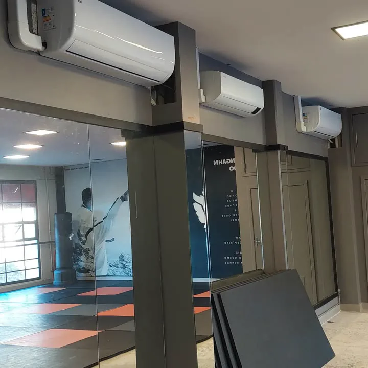 Três aparelhos split instalados no alto de um espaço comercial com paredes de vidro